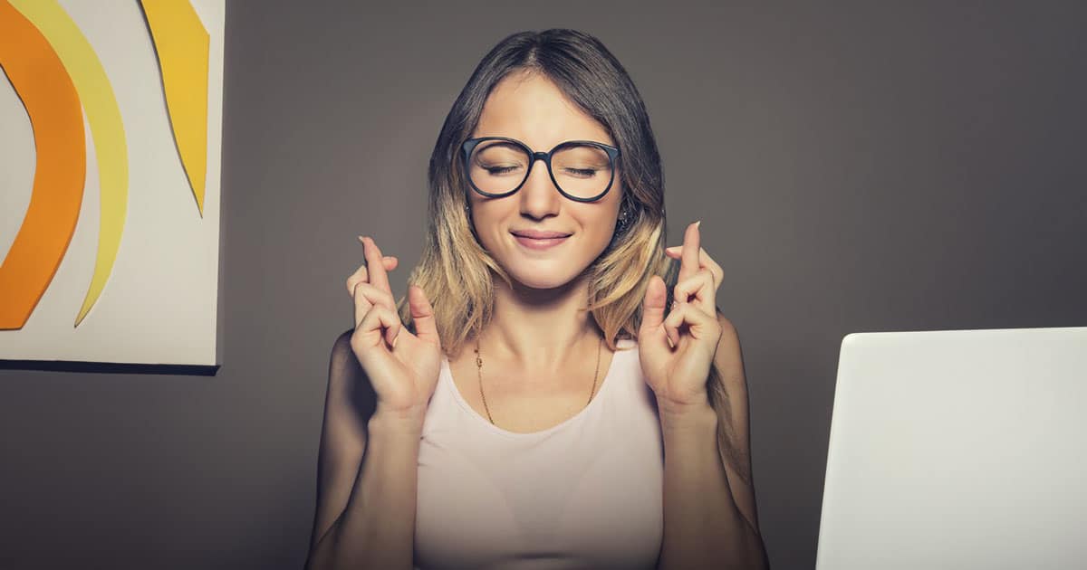 Young woman with eyes closed and fingers crossed